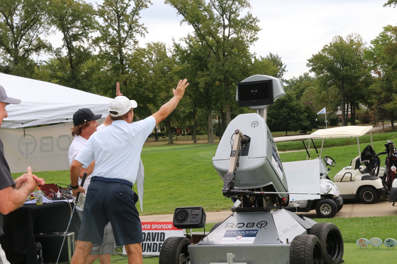 Two guests raise their arms in celebration next to Rob-OT at a charity tournament tee