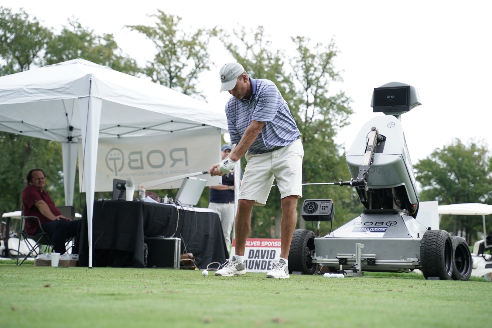 Guest teeing off next to Rob-OT with the ROB-OT tent behind him at a charity outing