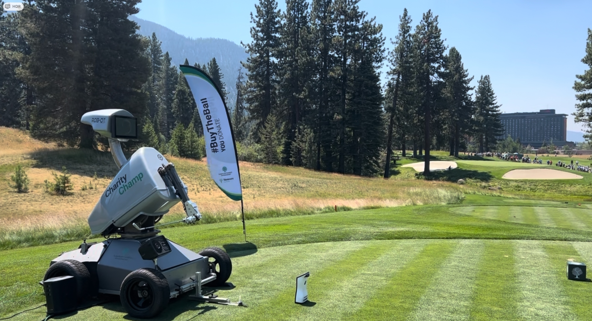 Rob-OT branded as Charity Champ on the tee at Edgewood Tahoe during the 2024 American Century Championship, with a #BuyTheBall banner beside him
